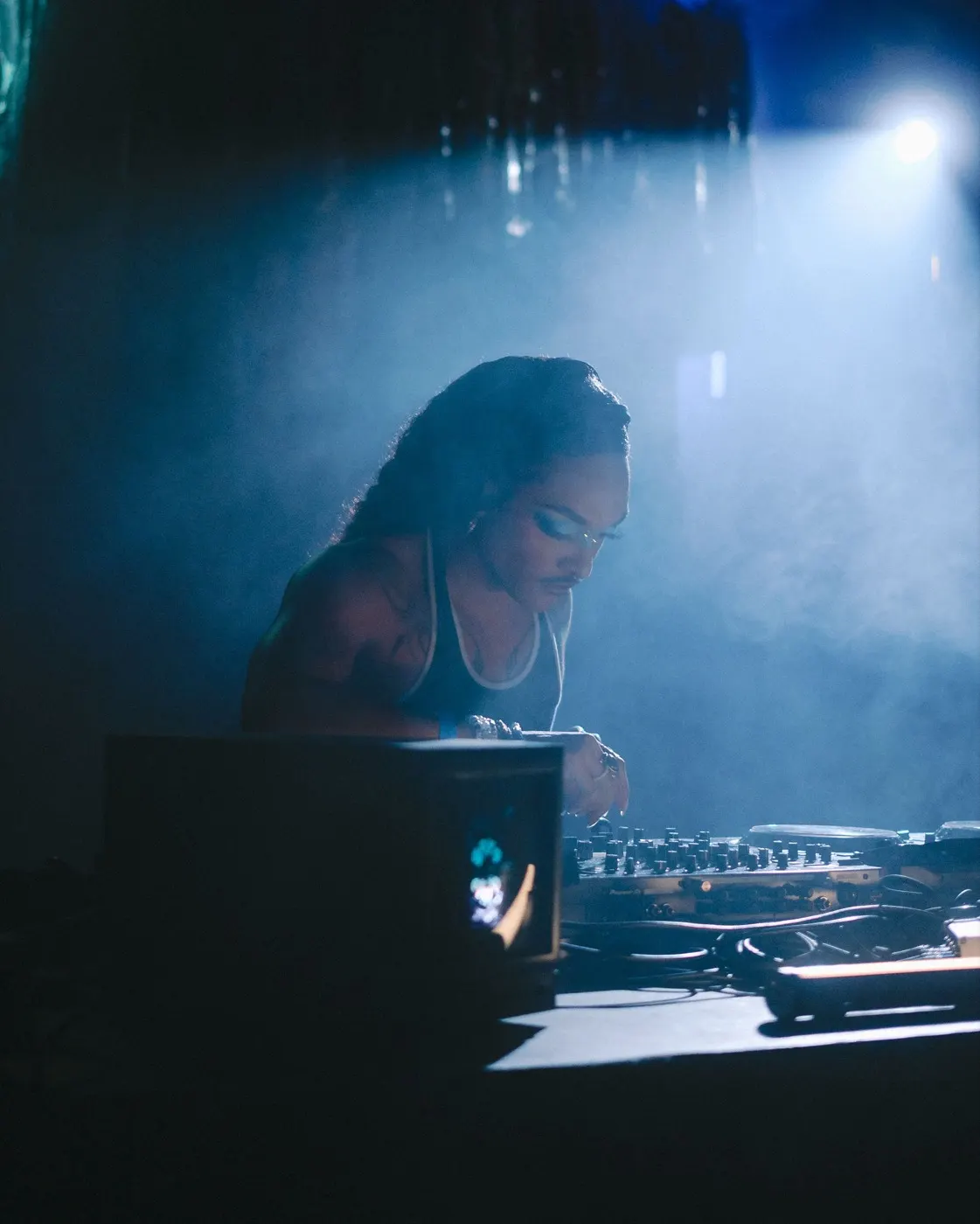 Woman DJ in a tank top focused on the mixer, warm light catching her face