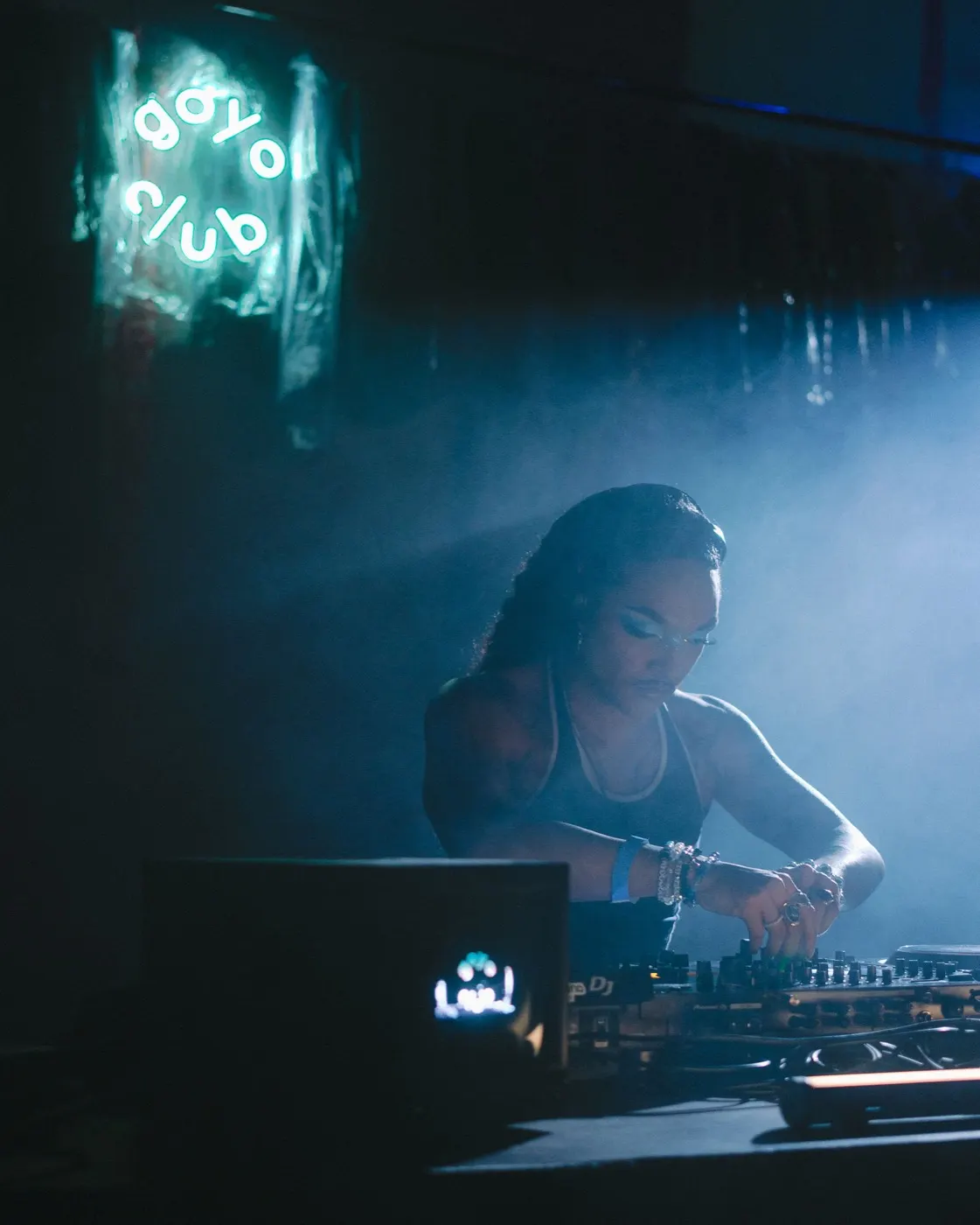 Woman DJ reaching for the mixer mid-set, blue stage light behind her