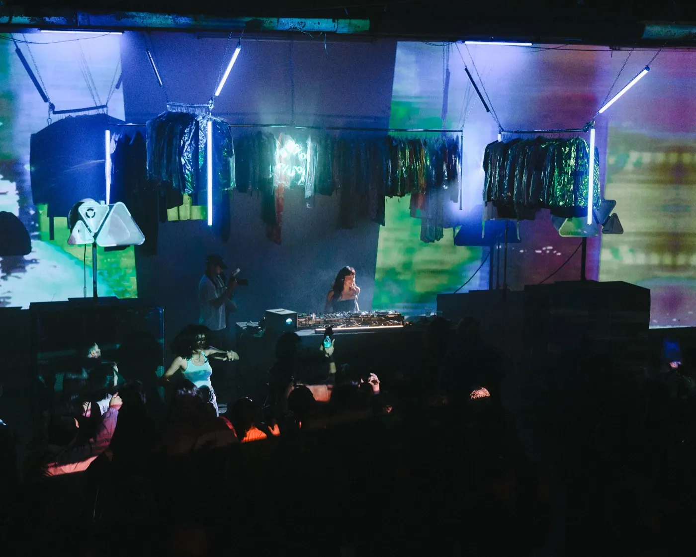 Wide shot of the booth and dancing crowd washed in pink and green light