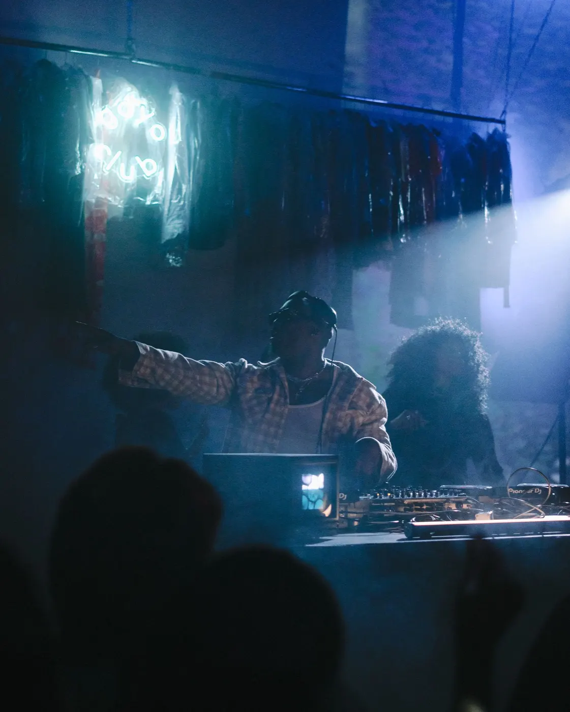 DJ with arms raised energetically, crowd silhouetted in the foreground