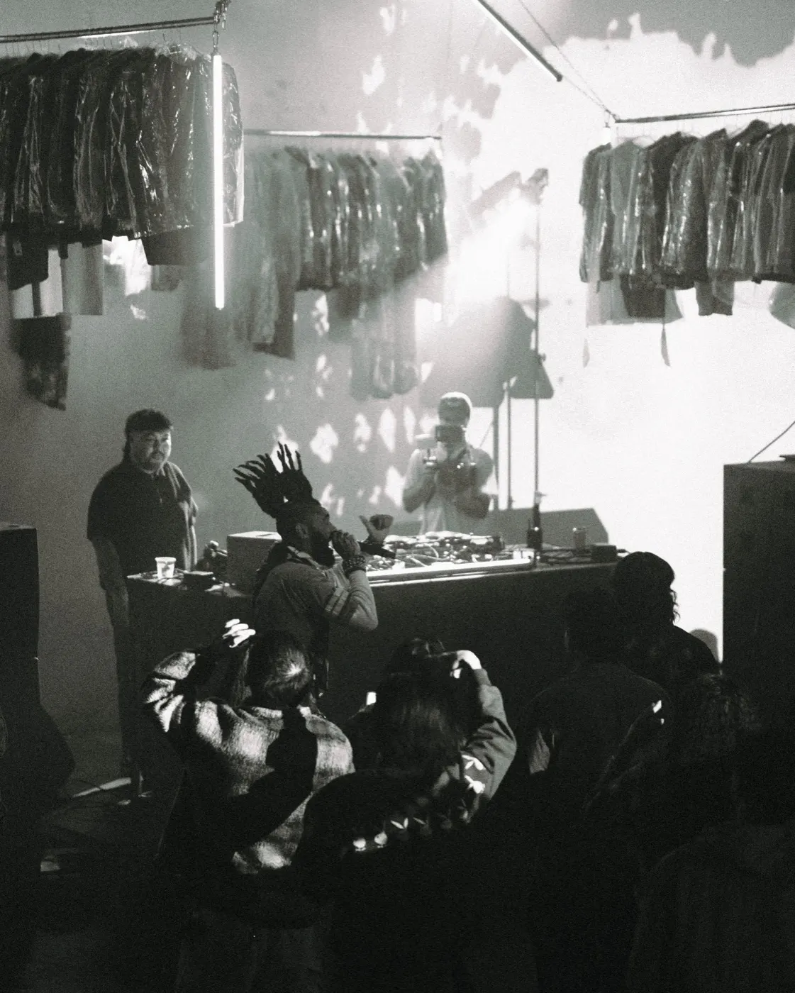 Black-and-white candid shot of a figure silhouetted among the hanging racks backstage