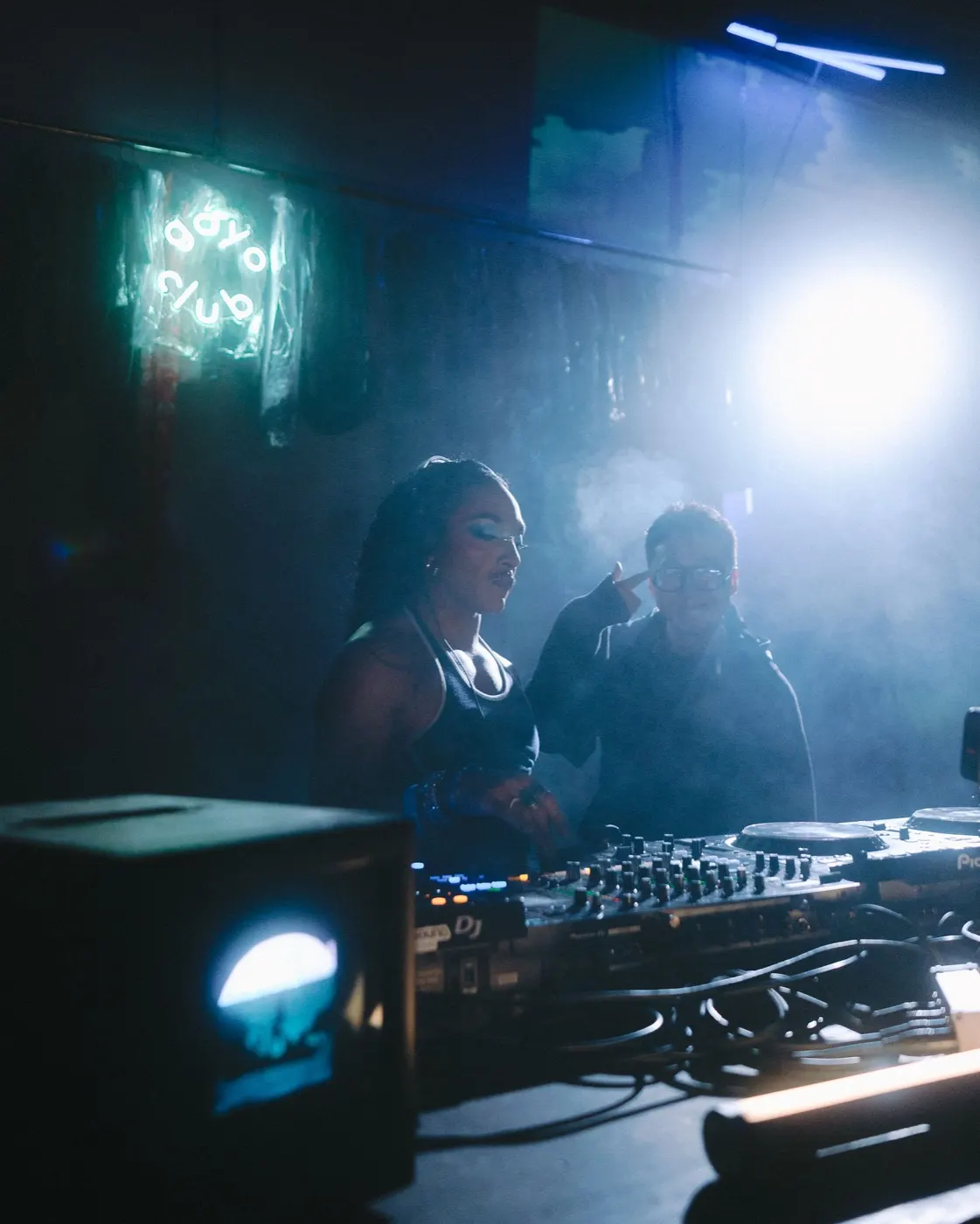 Woman DJ with headphones on, bright backlight flaring behind her