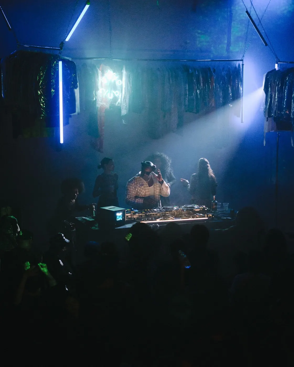 Wide shot of the DJ booth with the garment rack backdrop in cool blue light