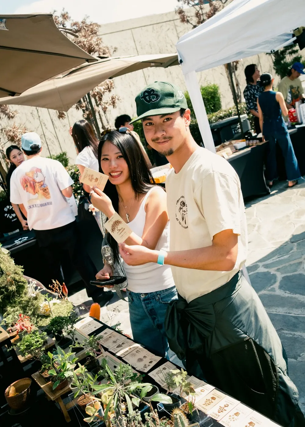 A vendor couple smiling behind a table of potted plants