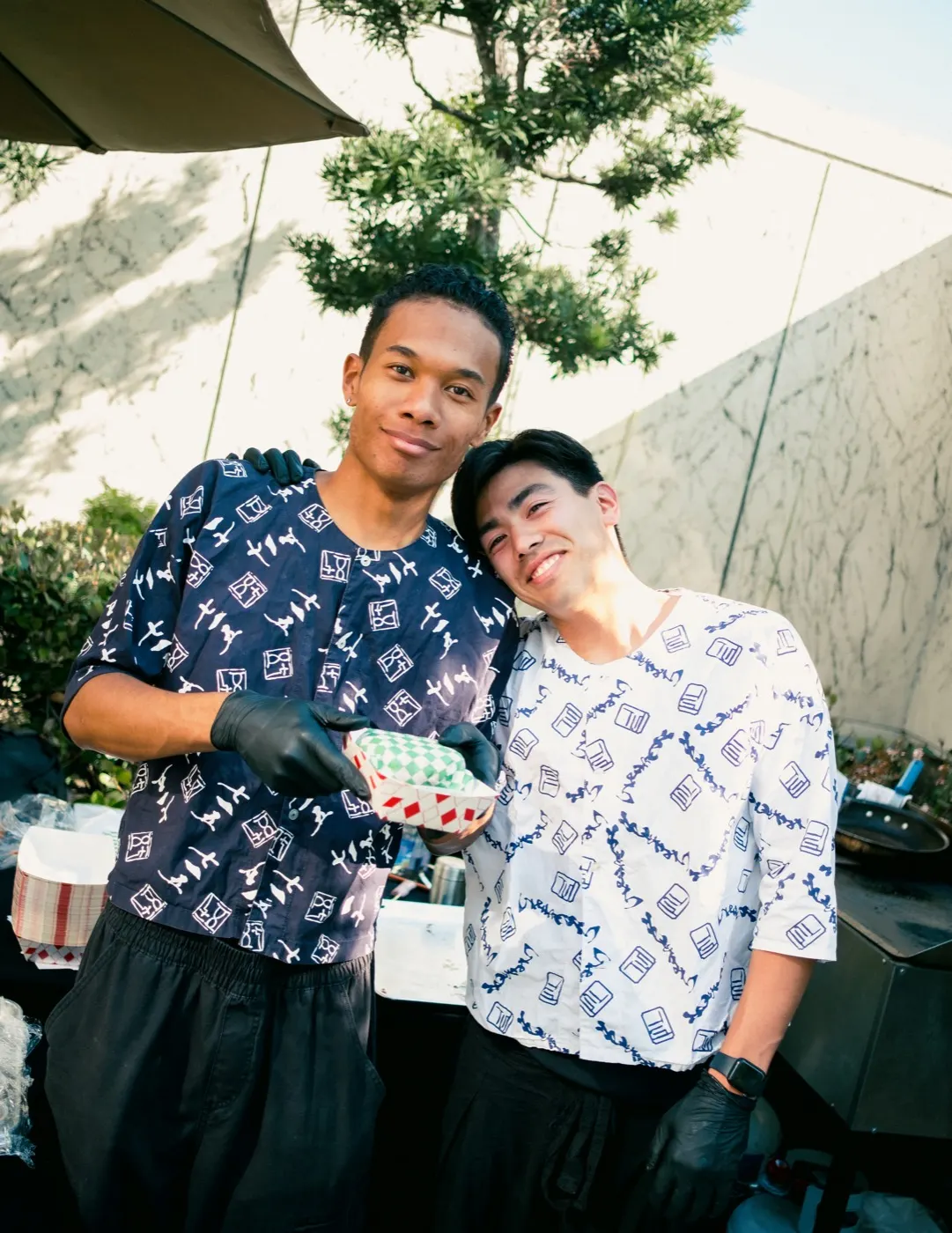 Two vendors in matching aprons smiling behind their table