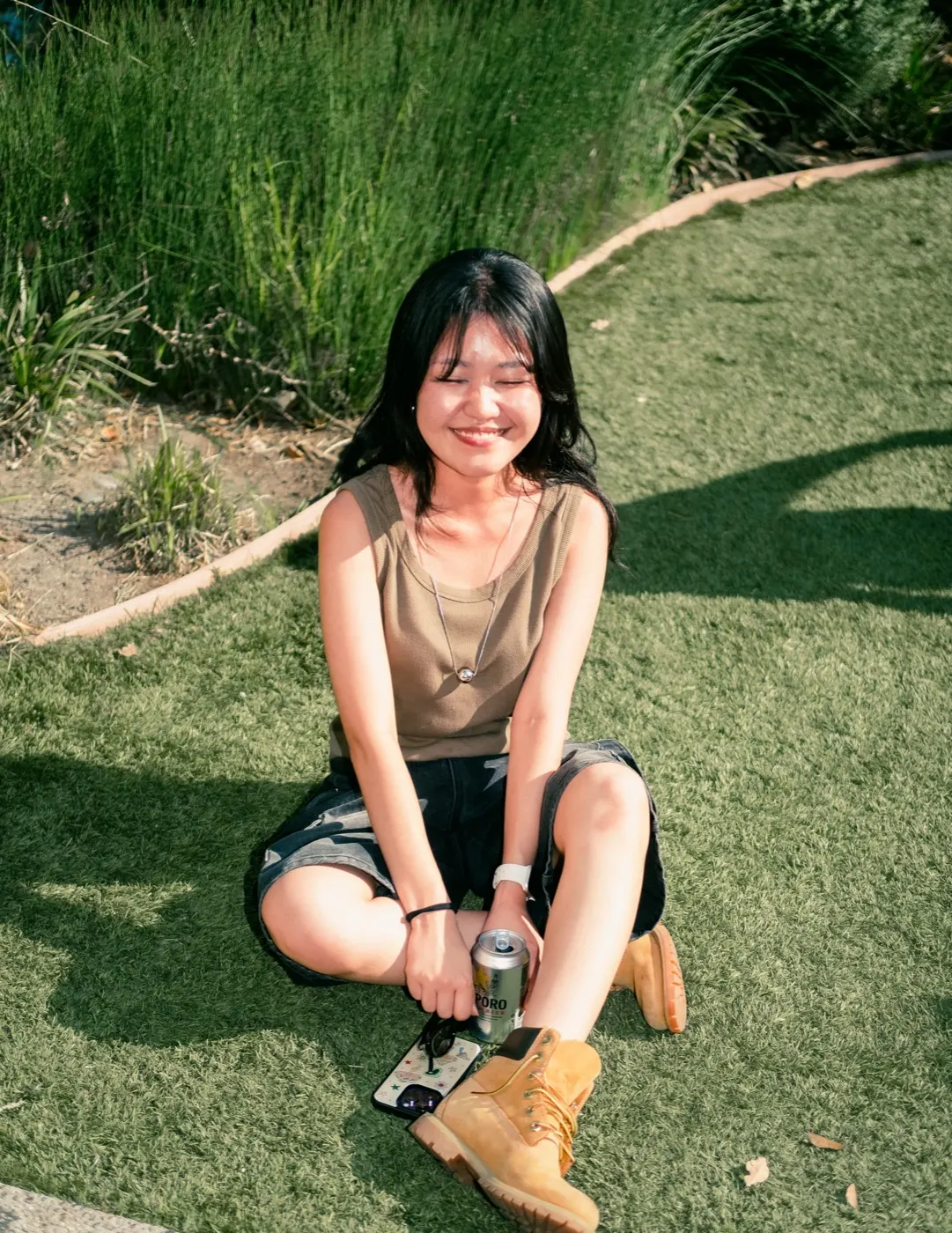 A guest sitting on the grass smiling, holding a drink