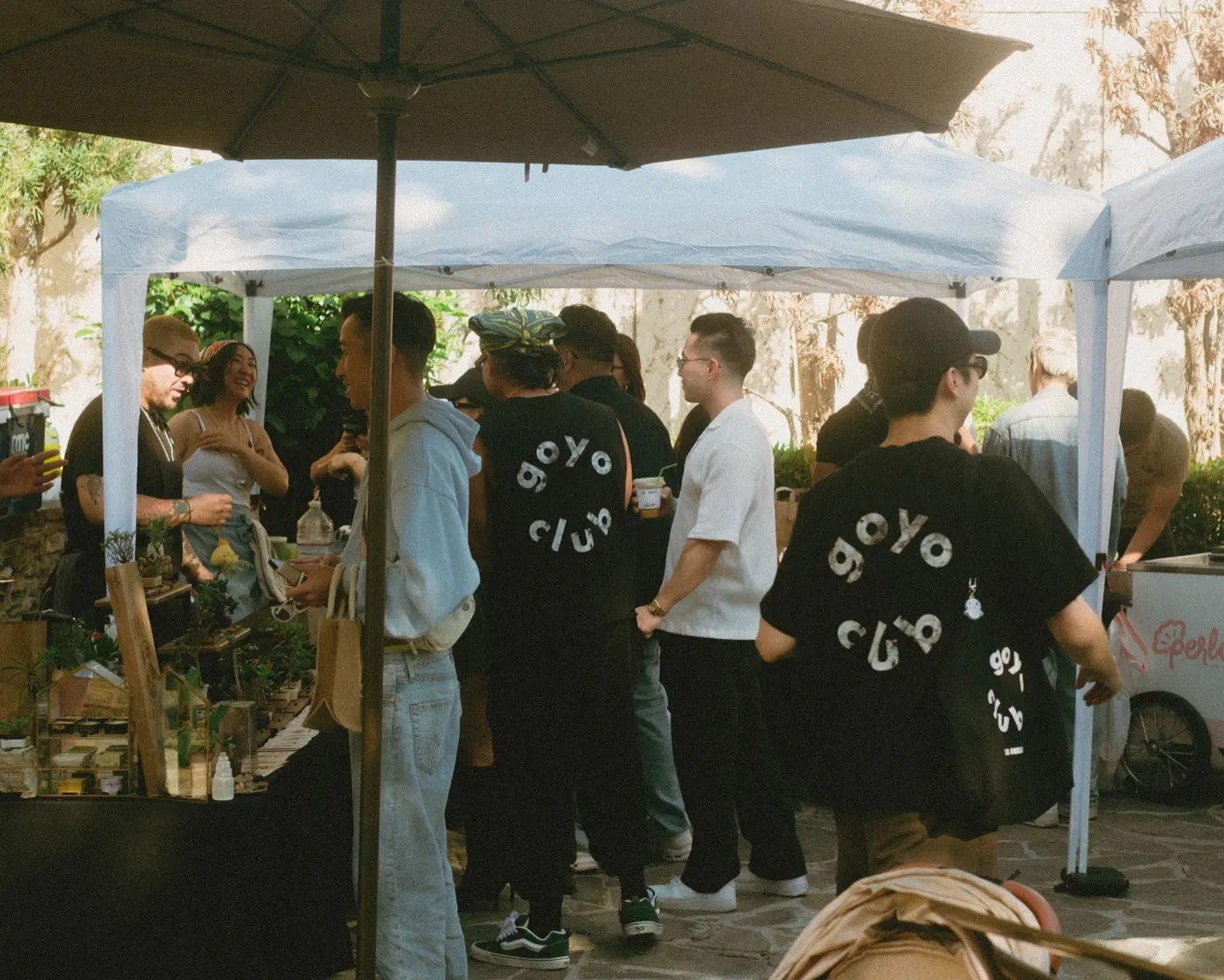 Group of attendees in black goyo club t-shirts posing together under a vendor tent
