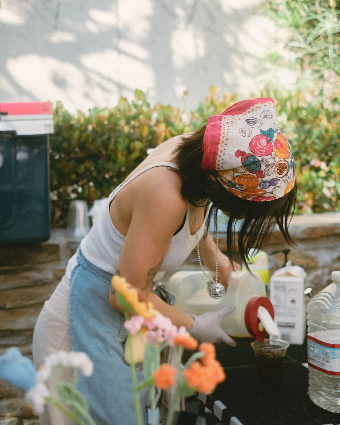 Close-up of hands preparing matcha at an outdoor table, wearing a floral bandana