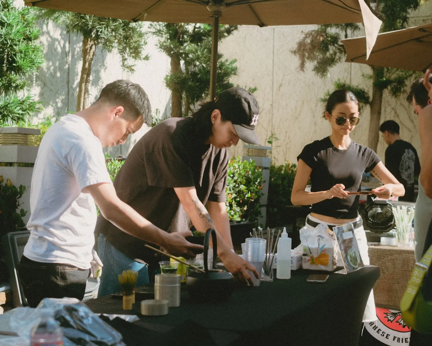 Three people whisking matcha and pouring drinks at an outdoor tasting table
