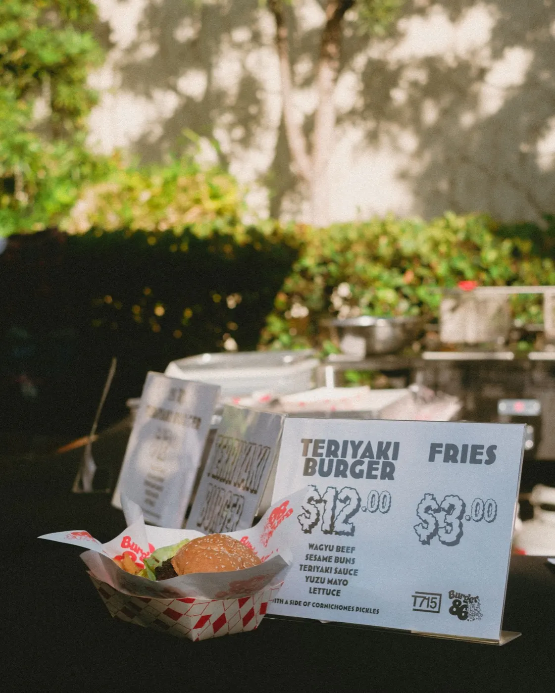 Close-up of a teriyaki burger and fries in a food tray next to the menu sign