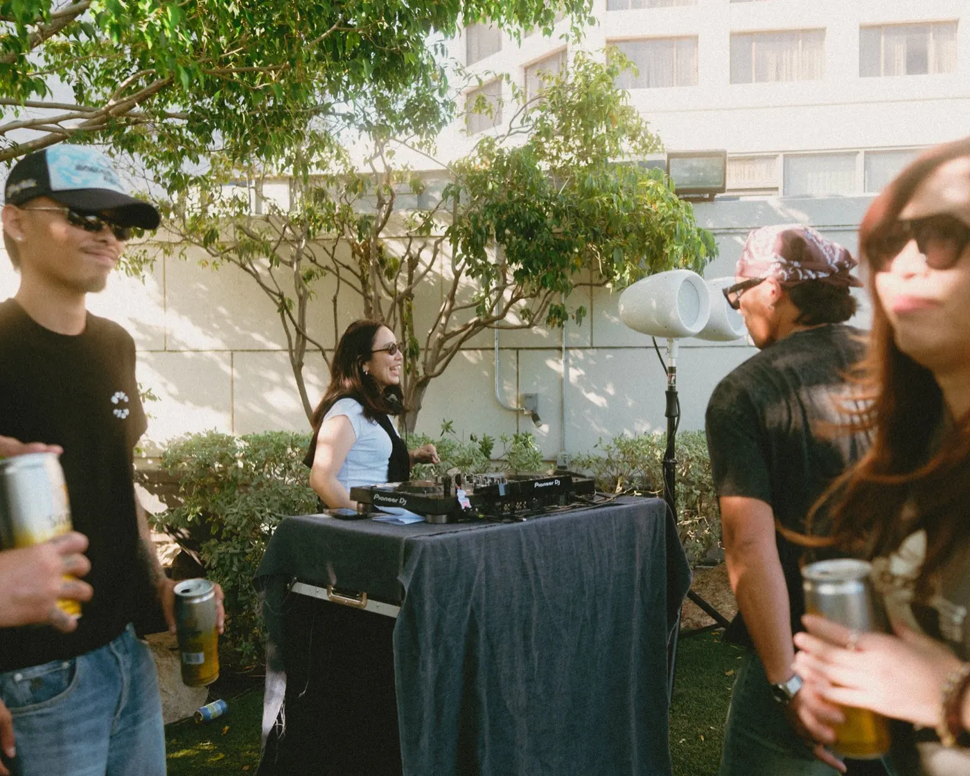 DJ smiling behind Pioneer turntables in the shade of the garden
