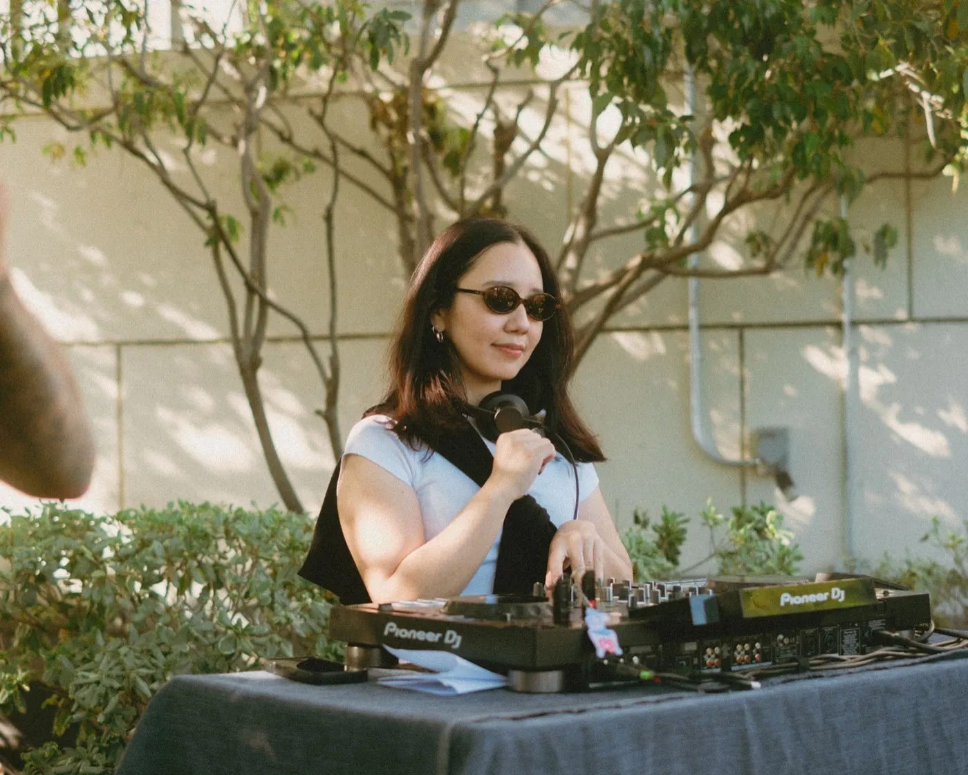 DJ holding a microphone at the decks with headphones around her neck
