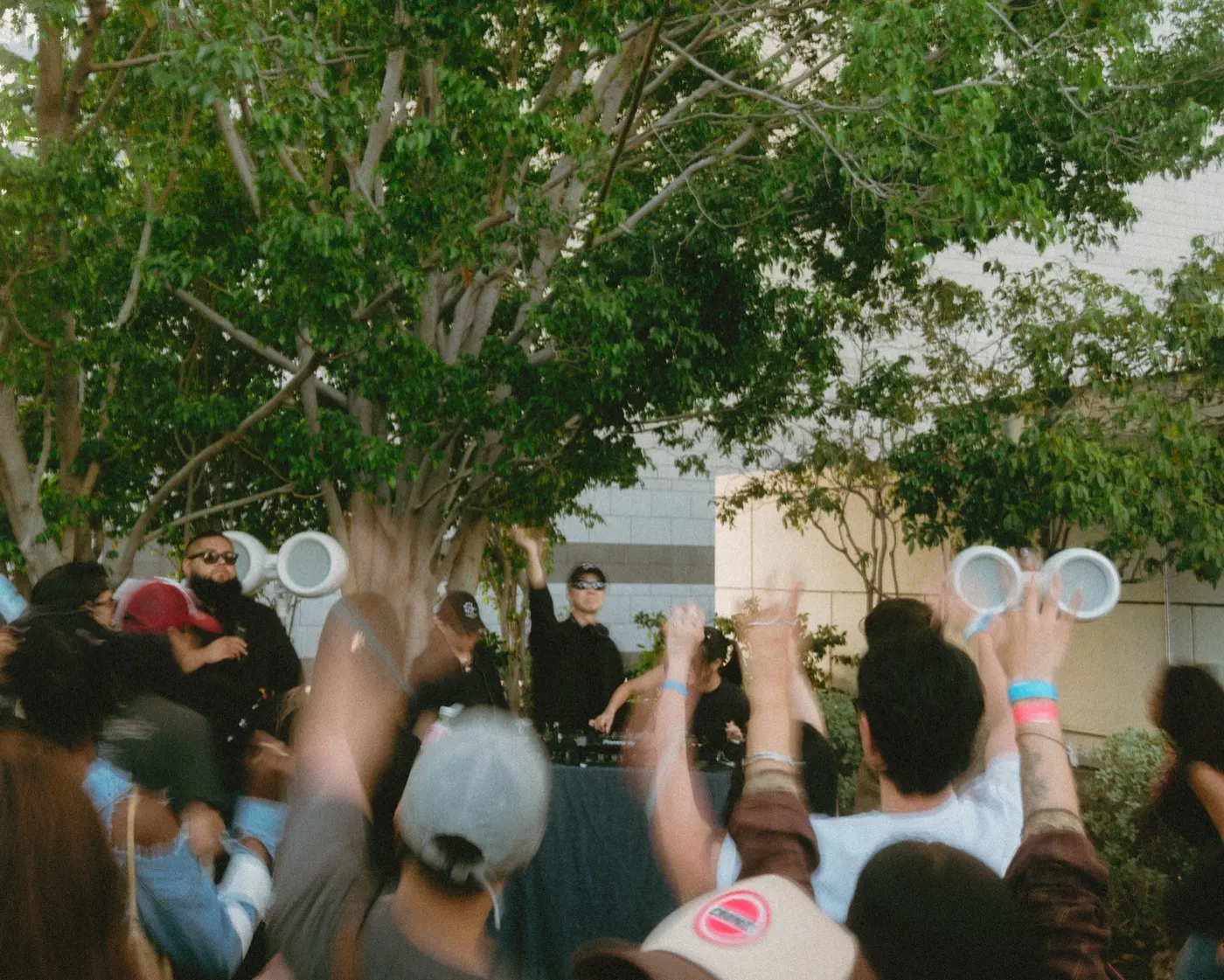 Crowd dancing with hands raised near the DJ booth and speaker stacks