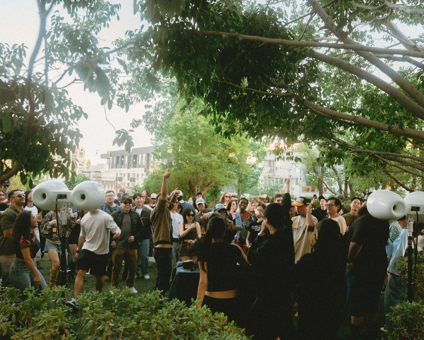 Crowd cheering and dancing under the trees near the sound system