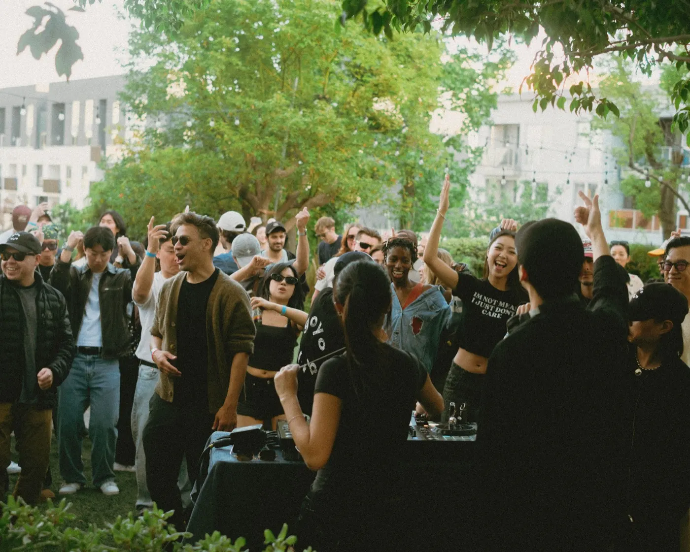 Energetic crowd with hands raised dancing around the DJ booth at dusk