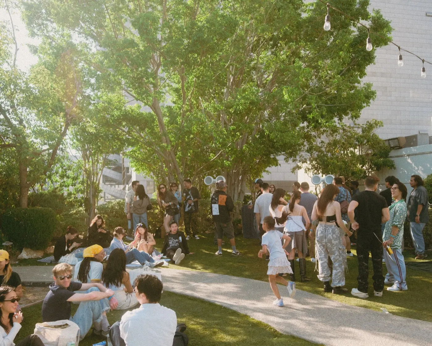 Crowd relaxing on the lawn as a child dances along the garden path